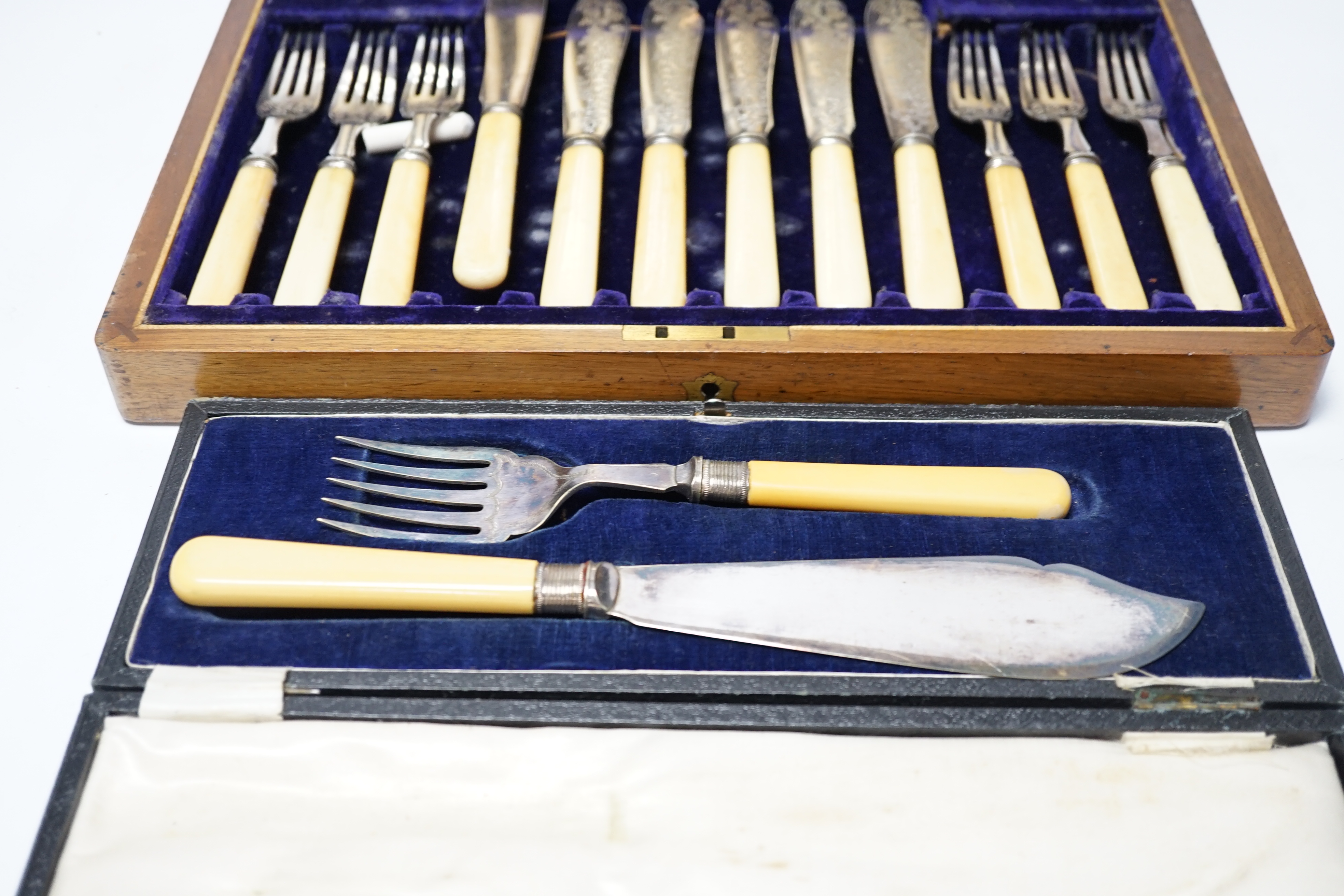 A set of twelve plated engraved fish knives and forks, with bone handles, cased together with a pair of plated fish servers with ivorine handles